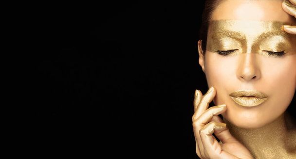 Beauty fashion model girl with holiday golden makeup. Beautiful woman with healthy glowing skin and shiny metallic gold make-up. Golden lips, eyes and nails. Isolated on black background - Zdjęcie, obraz