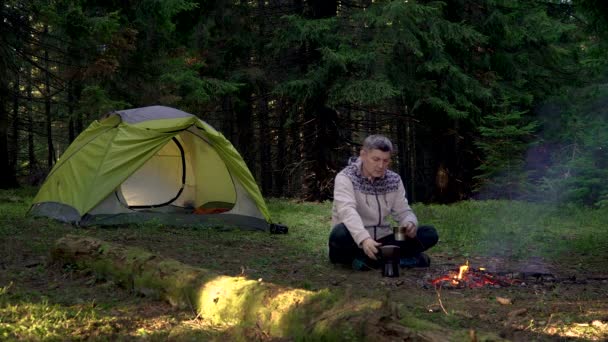 Un uomo beve caffè vicino a una tenda nella foresta - Filmati, video