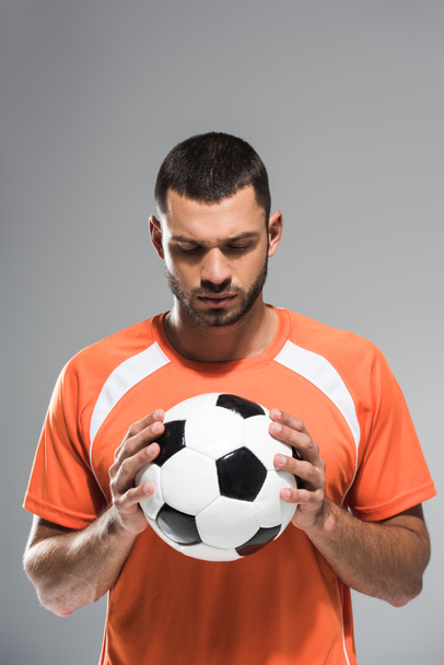 Brunette sportsman looking at football in hands isolated on grey - Fotó, kép
