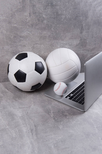 Soccer, volleyball and baseball ball and grey laptop on grey background. Online workout concept - Photo, Image