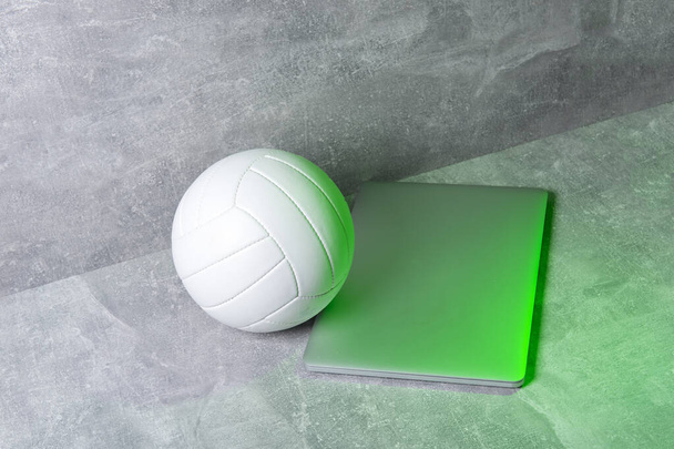Білий волейбол і сірий ноутбук на сірому тлі. Концепція онлайн тренування - Фото, зображення
