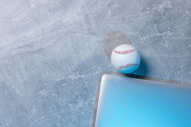 Beyzbol topu ve gri arka planda gri dizüstü bilgisayar. Çevrimiçi çalışma kavramı - Fotoğraf, Görsel