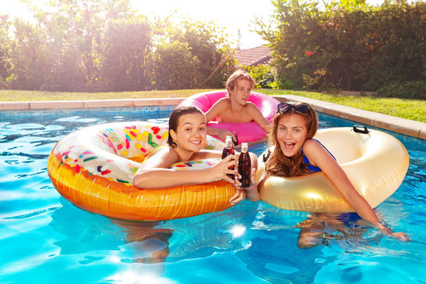 Three children float on inflatable toys and party drinking soda, laughing in the swimming pool - Photo, Image