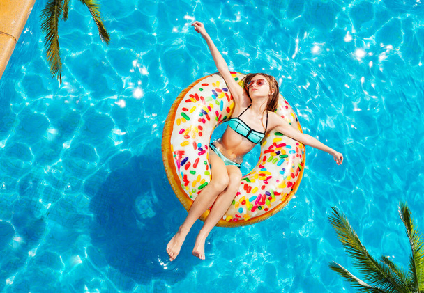 View from above of happy teen girl swim on inflatable yellow ring with spread hands on tropical resort - 写真・画像