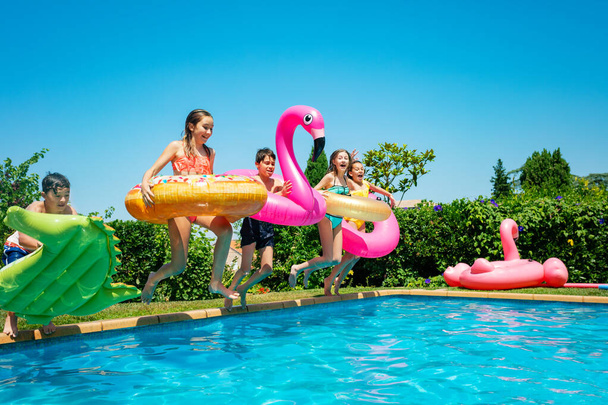 Group of children with inflatable toys donut run and jump in the water pool smiling happily spending vacations - Photo, image