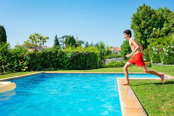 Tiener jongen lopen in het zwembad uitzicht van opzij in de tuin tijdens de zomervakantie - Foto, afbeelding