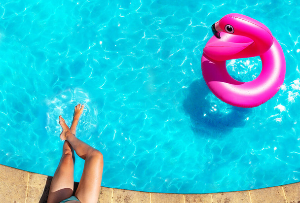 Woman's legs on the border and inflatable flamingo buoy swim in the swimming pool view from above - Foto, immagini