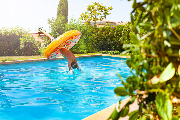 Happy boy dive in the swimming pool inside the doughnut inflatable toy - Foto, Bild