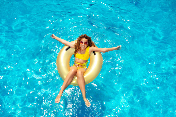 Beautiful teen girl swim in pool on inflatable doughnut view from above with hands apart and big smile - Фото, зображення