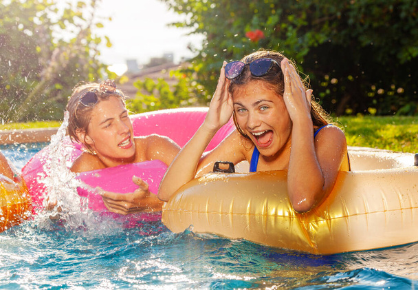 Two teens boy and girl play laughing in swimming pool splashing with inflatable toys - Foto, imagen