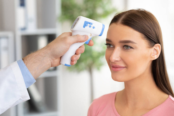 Lääkäri tarkistaa lämpötila nainen käyttää infrapuna lämpömittari - Valokuva, kuva