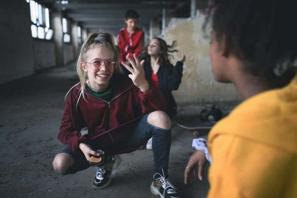 Group of teenagers gang sitting indoors in abandoned building, using smartphones. - Photo, Image