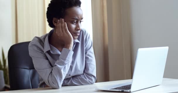 Traurig müde Afrikanerin arbeitet Laptop im Büro. Unzufriedene Frauen nutzen Computertechnologie zu Hause. Besorgte Mischlingshündin empfindet Stress bei freier Arbeit. Verärgerte Geschäftsfrau blickt auf Bildschirm - Filmmaterial, Video