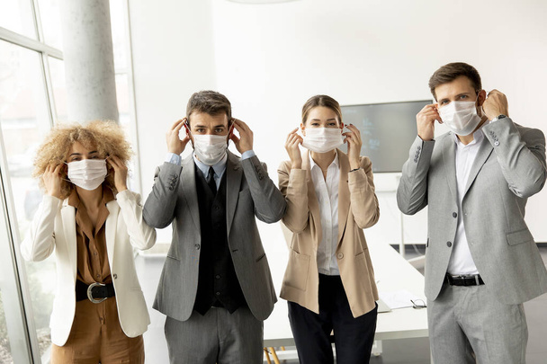 Business team togliersi la maschera protettiva per il viso e guardare la fotocamera in ufficio - Foto, immagini