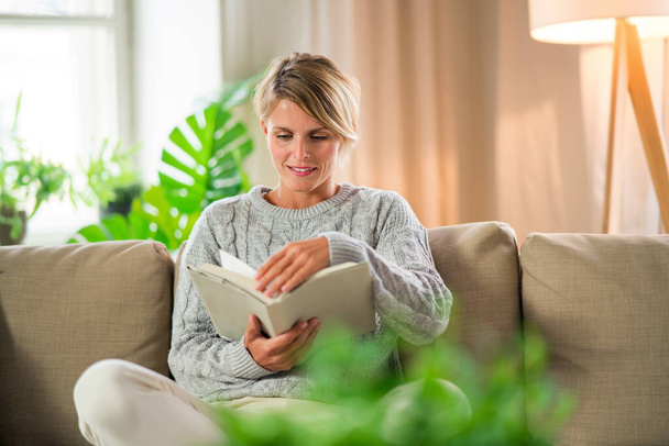 Portrait of woman relaxing with book indoors at home, mental health care concept. - Valokuva, kuva