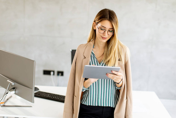 Jolie jeune femme d'affaires tenant tablette numérique et debout dans le bureau moderne - Photo, image