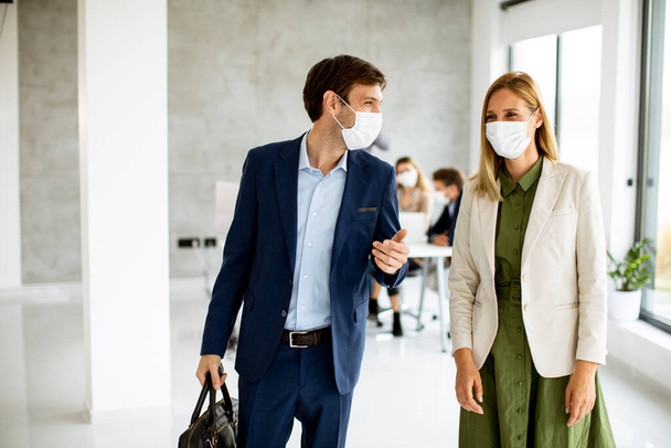 Bonito jovem casal de negócios andando juntos enquanto usam máscaras protetoras para evitar corona viruus no espaço de escritório - Foto, Imagem