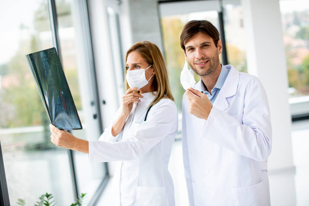 Команда врачей осматривает рентген, пока врач-мужчина снимает защитную маску для лица в медицинском кабинете - Фото, изображение