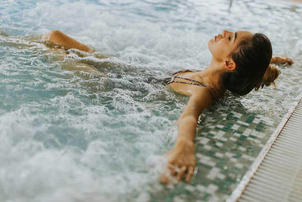 Ładna młoda kobieta relaksująca się w wannie z hydromasażem przy basenie - Zdjęcie, obraz