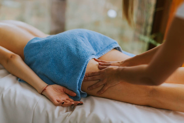 Beautiful young woman lying and having leg massage in spa salon during winter season - Foto, imagen