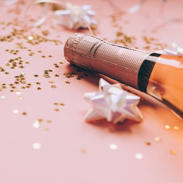 ピンクのパステル、サイドビューにローズシャンパンと黄金の光沢のある輝きスターコンフェッティのボトルとクリスマスや新年の組成物。パーティーお祝いの創造的なコンセプト - 写真・画像