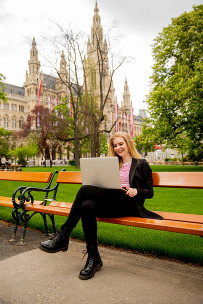 Young woman with laptop on the bench in the park in Vienna, Austria - 写真・画像