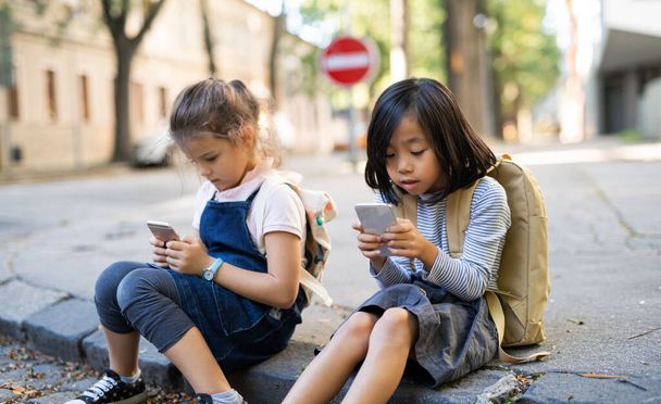 Small girls with smartphones outdoors in town, playing. - Foto, Imagen
