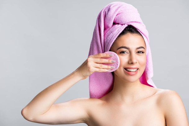 χαμογελαστή όμορφη γυναίκα με πετσέτα στα μαλλιά χρησιμοποιώντας σφουγγάρι απομονώνονται σε γκρι - Φωτογραφία, εικόνα