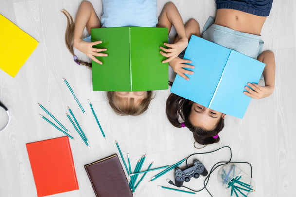 люди, діти, друзі, література та концепція дружби - дві щасливі дівчата лежать на підлозі та читають книгу вдома
 - Фото, зображення