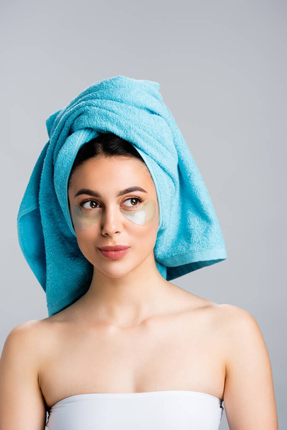 όμορφη γυναίκα με μπλε πετσέτα στα μαλλιά και κηλίδες υδρογέλης στο πρόσωπο απομονώνονται σε γκρι - Φωτογραφία, εικόνα