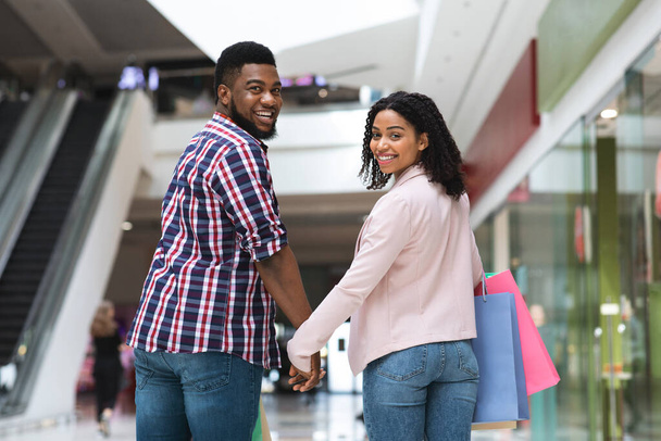 Rozrywka dla par. Czarny mężczyzna i kobieta spacerujący w centrum handlowym, trzymając się za ręce - Zdjęcie, obraz