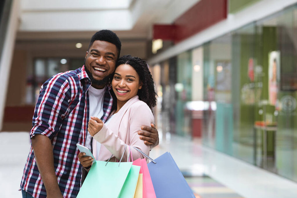 Wesoły czarny małżonkowie pozowanie w centrum handlowym po udanym zakupy, dokonywania zakupów razem - Zdjęcie, obraz