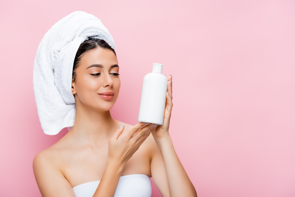 beautiful woman with towel on hair and bottle of lotion isolated on pink - Фото, изображение