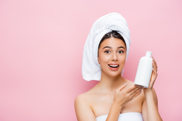 happy beautiful woman with towel on hair and bottle of lotion isolated on pink - Photo, image