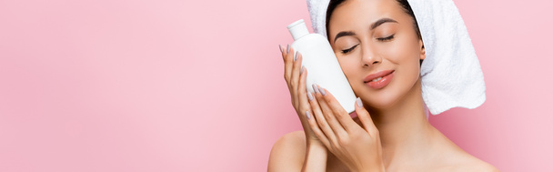 beautiful woman with closed eyes, towel on hair and bottle of lotion isolated on pink, banner - Photo, Image