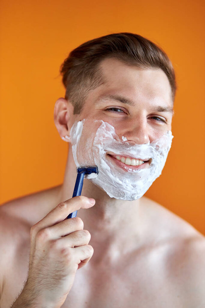 caucasian man with white foam on his face, isolated on orange background - 写真・画像