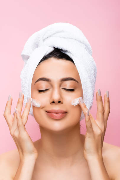 beautiful woman with towel on hair, closed eyes and cosmetic cream on face isolated on pink - Φωτογραφία, εικόνα
