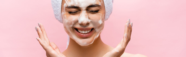 usmívající se krásná žena s ručníkem na vlasech a pěnou na tváři izolované na růžové, banner - Fotografie, Obrázek