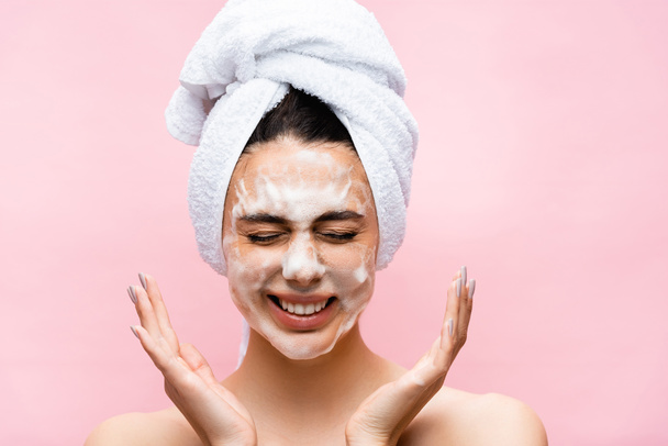 smiling beautiful woman with towel on hair and foam on face isolated on pink - Fotoğraf, Görsel