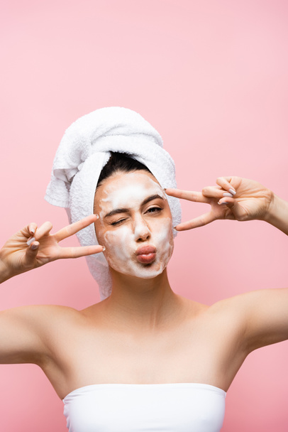 beautiful woman with towel on hair and foam on face grimacing isolated on pink - Foto, immagini