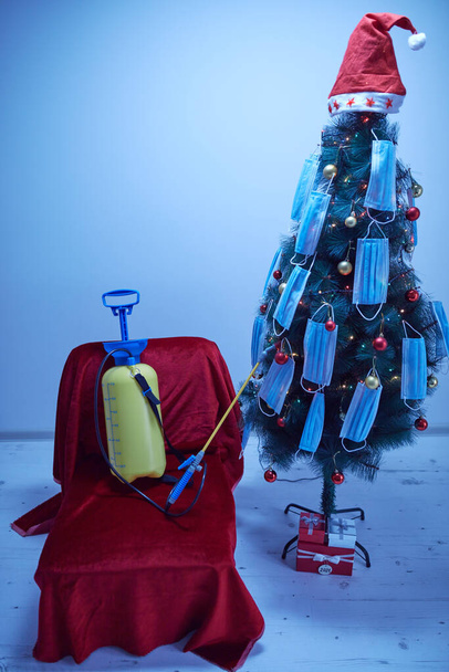Esperando Navidad y Año Nuevo en cuarentena durante la pandemia de Covid 19 / Coronavirus. Pulverizador para descontaminar gérmenes en una silla roja junto a un árbol decorado. - Foto, imagen