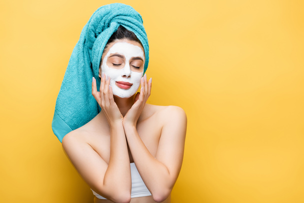 beautiful woman with closed eyes, blue towel on hair and clay mask on face isolated on yellow - Foto, Imagem