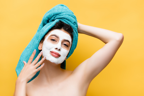 beautiful woman with blue towel on hair and clay mask on face isolated on yellow - Foto, Imagen