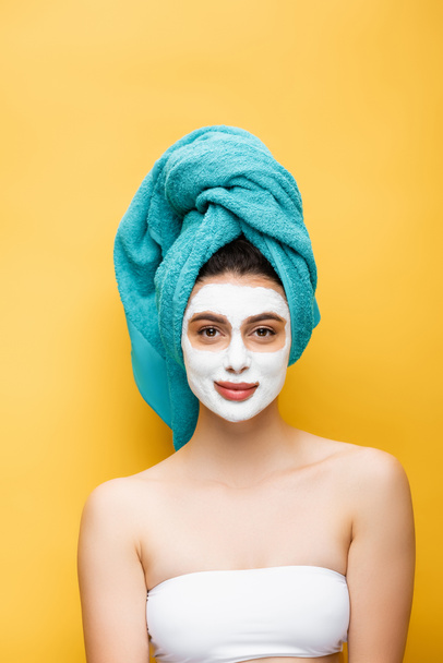 beautiful woman with blue towel on hair and clay mask on face isolated on yellow - Fotografie, Obrázek