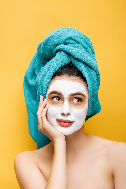 beautiful woman with blue towel on hair and clay mask on face isolated on yellow - Foto, Bild