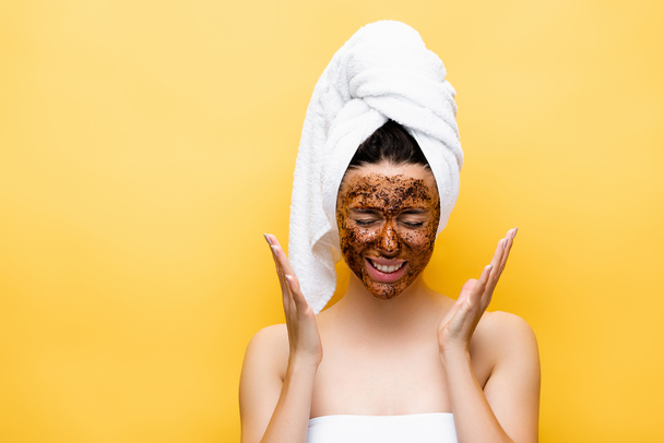 beautiful woman with towel on head and coffee mask on face isolated on yellow - Foto, Imagen