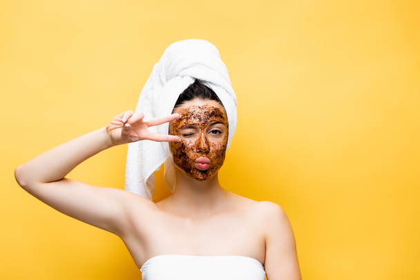beautiful woman with towel on head and coffee mask on face grimacing isolated on yellow - Foto, Imagem