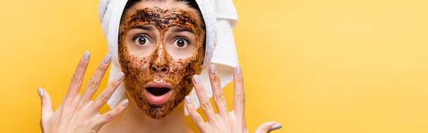 shocked beautiful woman with towel on head and coffee mask on face isolated on yellow, banner - Foto, Imagem