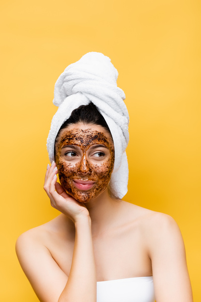 beautiful woman with towel on head and coffee mask on face isolated on yellow - Photo, Image