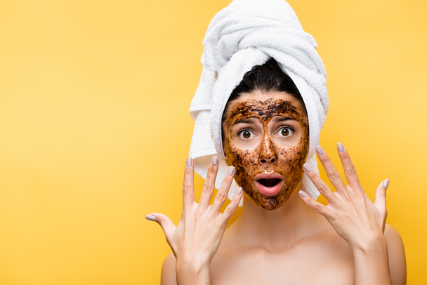 shocked beautiful woman with towel on head and coffee mask on face isolated on yellow - Foto, immagini